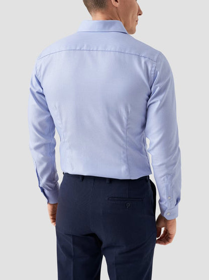A man seen from behind wears the Eton Slim Fit Semi Solid Dobby Dress Shirt in Light Blue with dark blue dress pants, set against a plain light background.