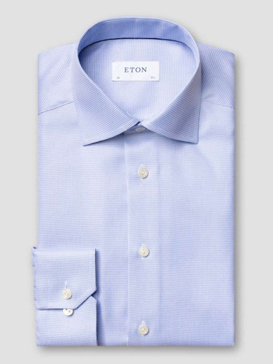 The Eton Slim Fit Semi Solid Dobby Dress Shirt in Light Blue, featuring a cut away collar and buttoned cuffs, is neatly folded and displayed against a plain gray background.