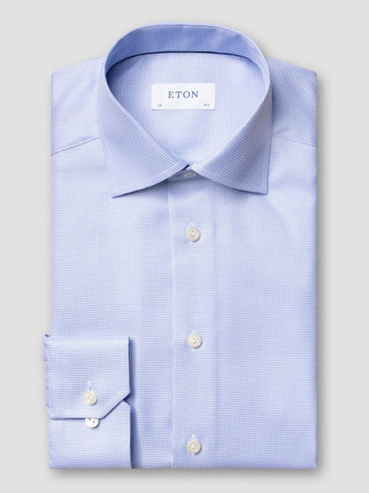 The Eton Slim Fit Semi Solid Dobby Dress Shirt in Light Blue, featuring a cut away collar and buttoned cuffs, is neatly folded and displayed against a plain gray background.