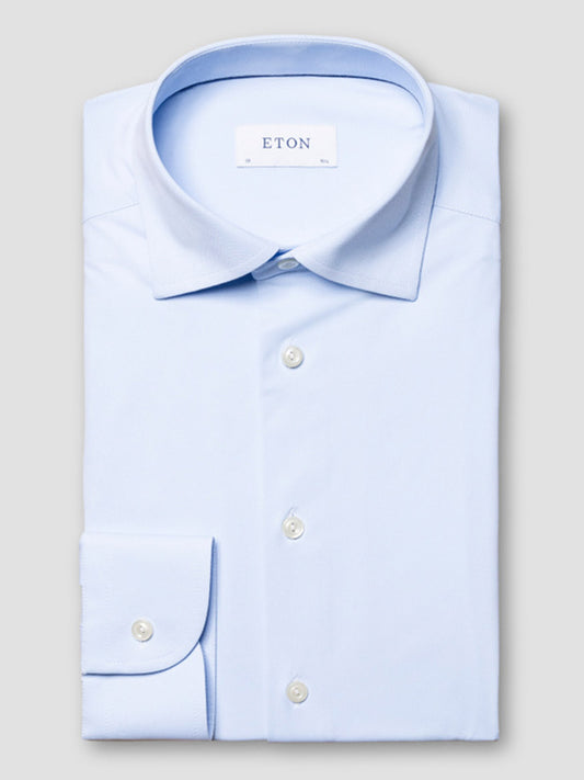 A neatly folded Eton Slim Fit Semi Solid Four-Way Stretch Shirt in light blue with white buttons and a visible "ETON" label inside the collar, displayed on a plain background.