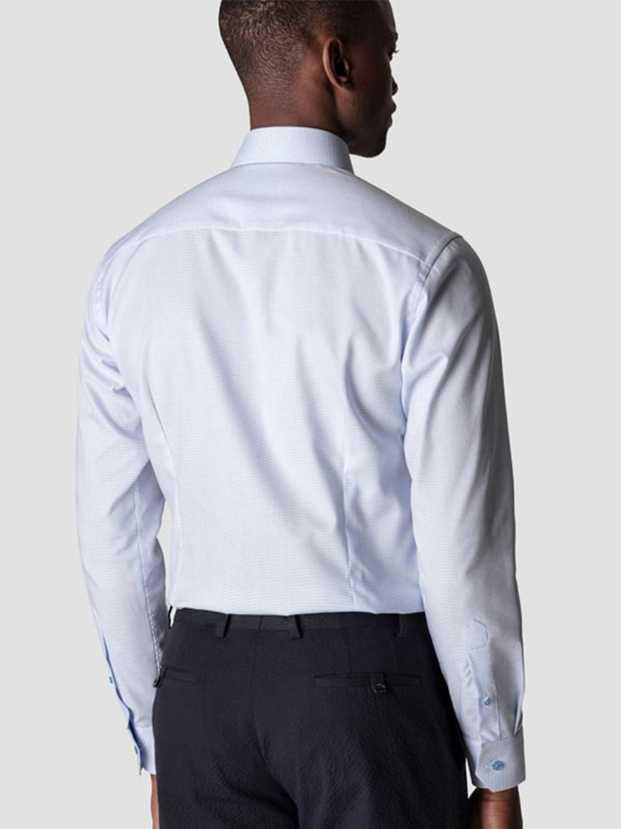 A man is seen from the back wearing the Eton Contemporary Fit Semi Solid Piping Details Shirt in light blue with dark trousers, set against a plain light gray background.