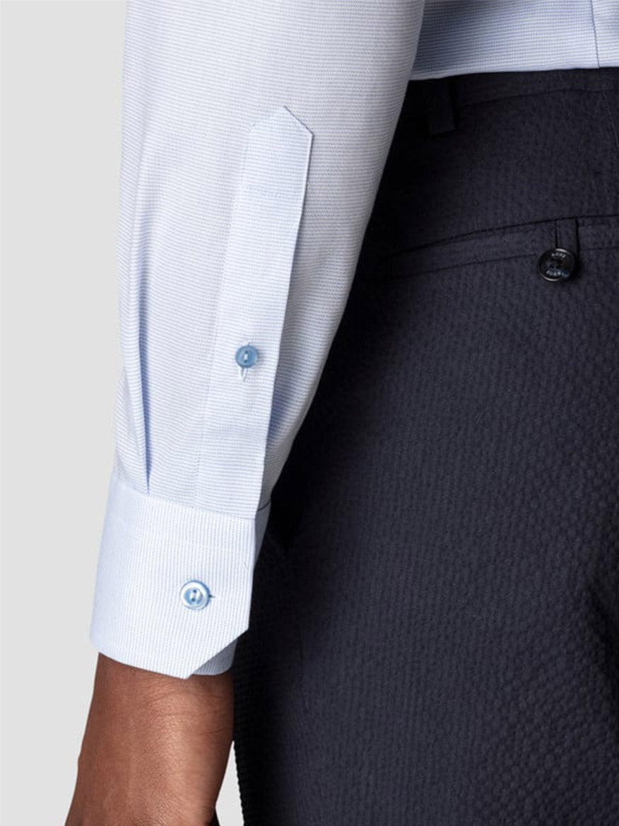 A close-up of a person wearing the Eton Contemporary Fit Semi Solid Piping Details Shirt in Light Blue with buttoned cuffs and dark textured dress pants, showcasing a refined, modern look.