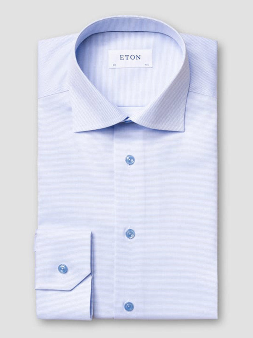 The Eton Contemporary Fit Semi Solid Piping Details Shirt in light blue features long sleeves, a spread collar, blue buttons, and is neatly folded with "ETON" labeled inside the collar.