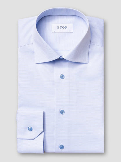 The Eton Contemporary Fit Semi Solid Piping Details Shirt in light blue features long sleeves, a spread collar, blue buttons, and is neatly folded with "ETON" labeled inside the collar.