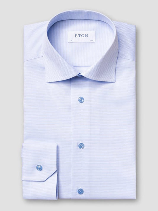 The Eton Contemporary Fit Semi Solid Piping Details Shirt in light blue features long sleeves, a spread collar, blue buttons, and is neatly folded with "ETON" labeled inside the collar.