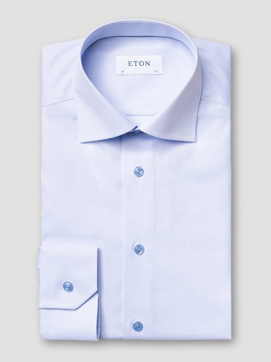 The Eton Slim Fit Semi Solid Piping Details Shirt in Light Blue features a cut away collar and blue buttons, neatly folded and labeled "Eton," displayed on a plain gray background.