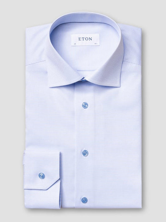 The Eton Slim Fit Semi Solid Piping Details Shirt in Light Blue features a cut away collar and blue buttons, neatly folded and labeled "Eton," displayed on a plain gray background.