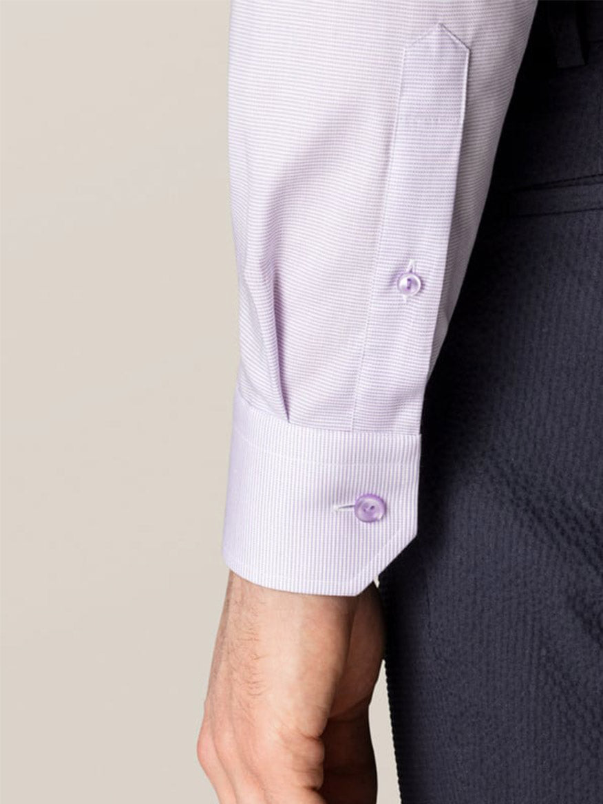 A close-up of a person’s left arm wearing the Eton Slim Fit Semi Solid Piping Details Shirt in Light Purple with buttoned cuffs and dark trousers, set against a plain beige background.