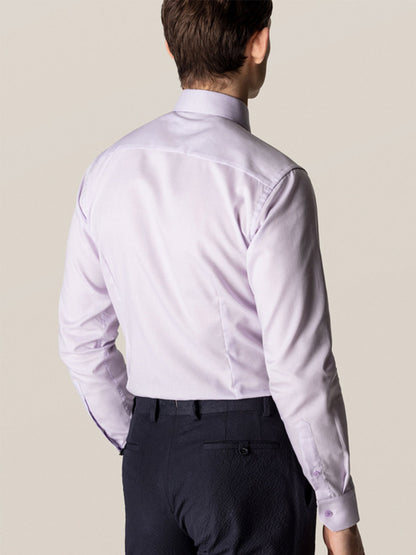 A man stands with his back to the camera against a plain background, wearing the Eton Contemporary Fit Semi Solid Piping Details Dress Shirt in light purple and dark trousers.