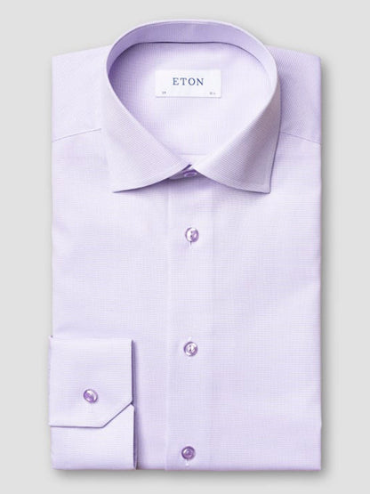 The Eton Contemporary Fit Semi Solid Piping Details Dress Shirt in Light Purple, featuring buttoned cuffs and a spread collar, is neatly folded and displayed against a plain gray background.