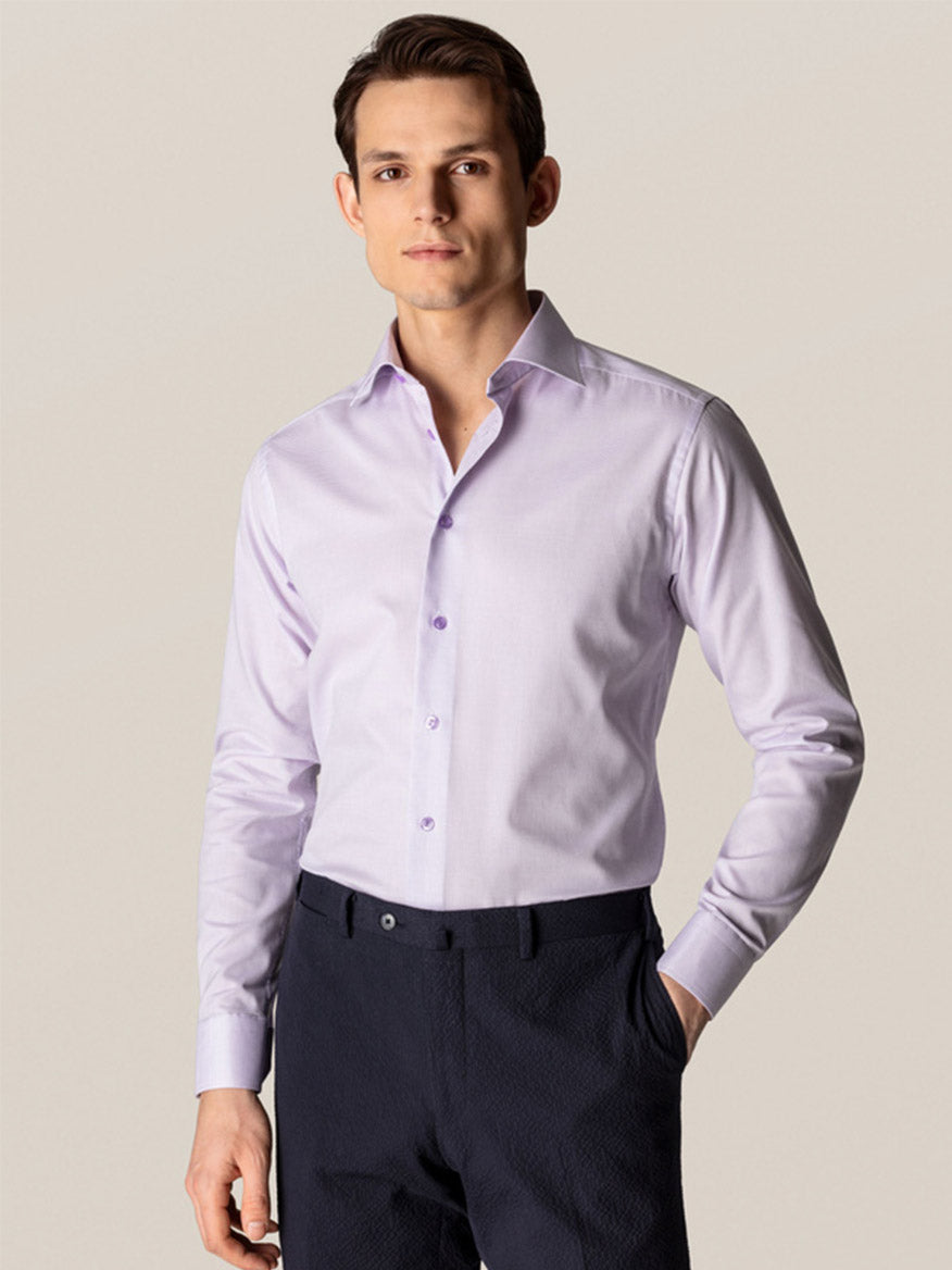 A man wears the Eton Contemporary Fit Semi Solid Piping Details Dress Shirt in light purple, paired with dark trousers, standing with one hand in his pocket against a neutral background.