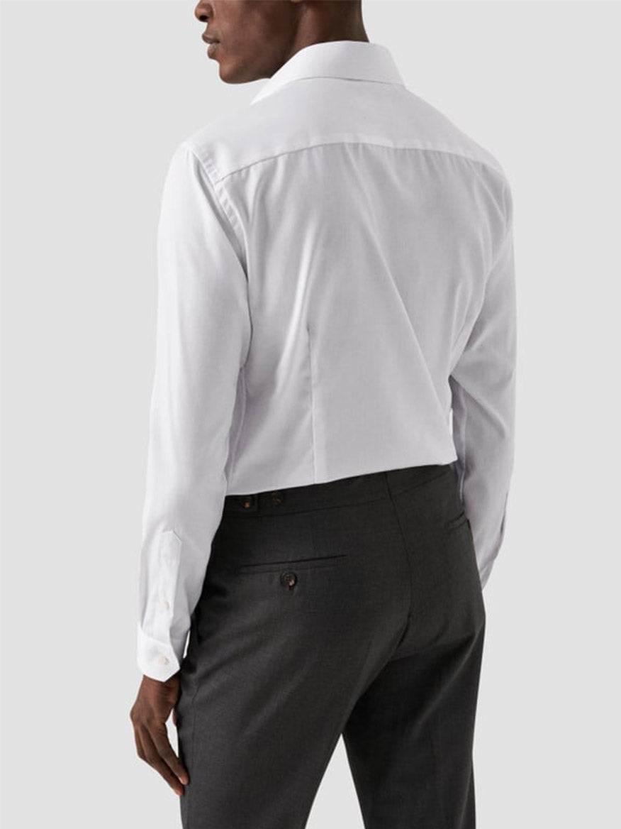 A man is seen from behind wearing an Eton Contemporary Fit White Signature Twill Dress Shirt and dark gray dress pants against a plain light gray background.
