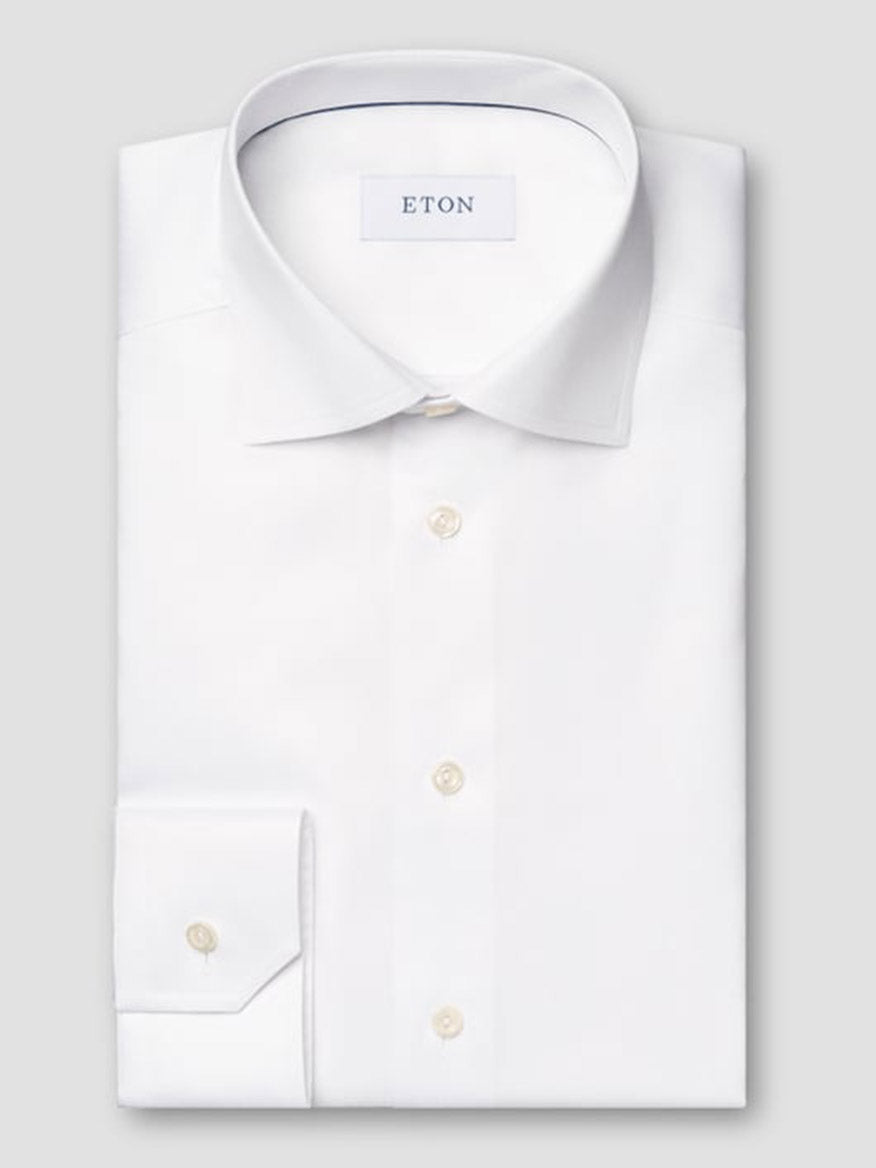 The Eton Contemporary Fit White Signature Twill Dress Shirt, featuring a pointed collar and buttoned cuffs, is neatly folded and displayed on a light gray background.