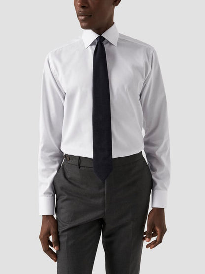 A person wearing an Eton Contemporary Fit White Signature Twill Dress Shirt, a dark tie, and gray dress pants stands against a plain light background.