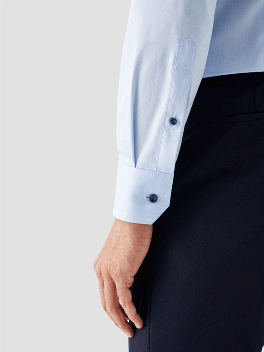 A person wears the Eton Contemporary Fit Signature Twill Dress Shirt in Light Blue with Navy Details and dark trousers, shown from the waist down with their arm relaxed at their side.