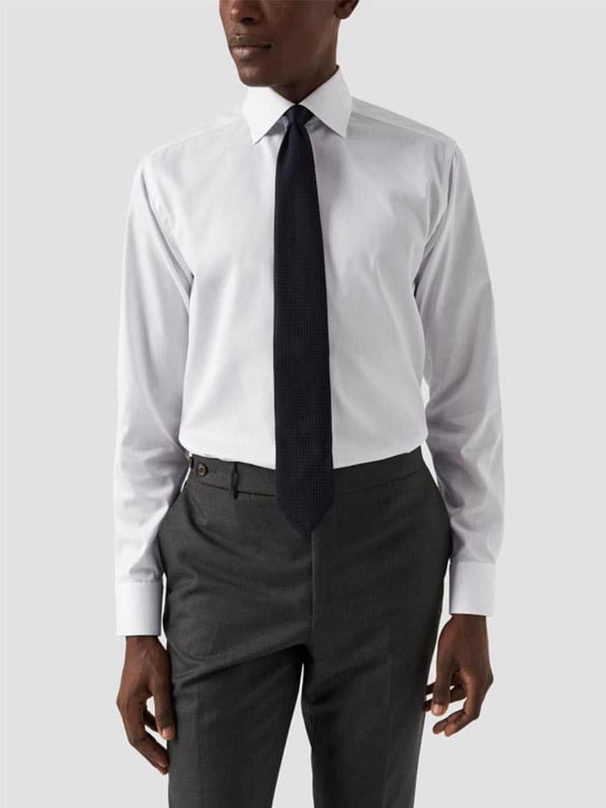 A person wears an Eton Slim Fit Solid Signature Twill Dress Shirt in White with a dark tie and gray trousers, standing against a plain light gray background.