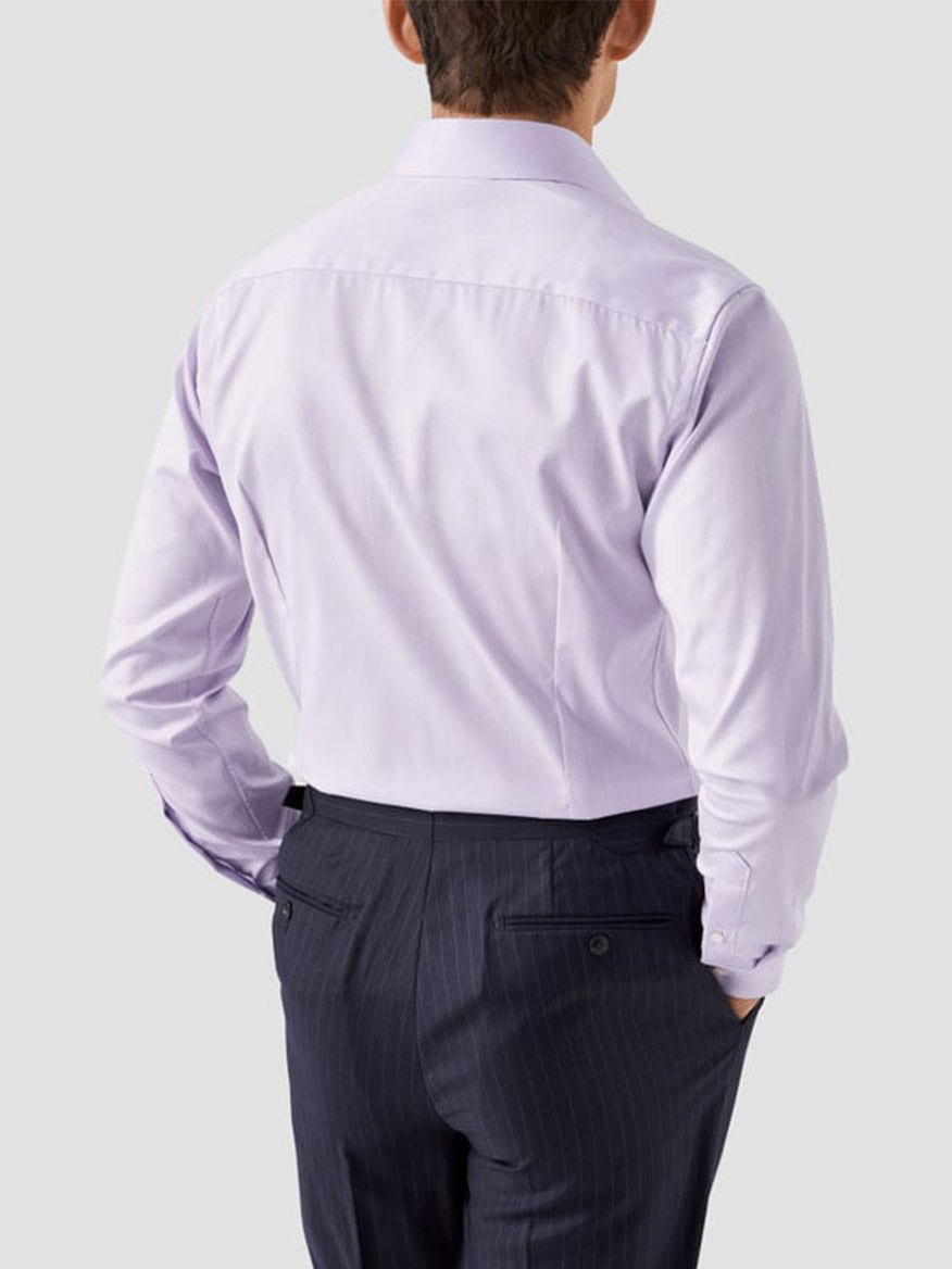 A man is seen from behind wearing the Eton Slim Fit Solid Signature Twill Dress Shirt in Mid Purple and dark pinstripe dress pants, standing against a plain light gray background.