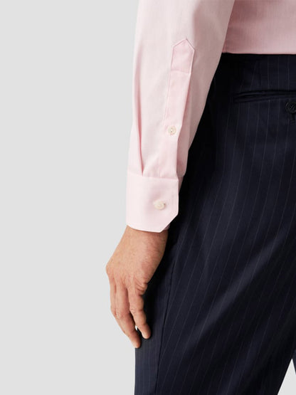 A person wears an Eton Slim Fit Solid Signature Twill Dress Shirt in Pink with dark pinstripe trousers, their arm resting by their side.