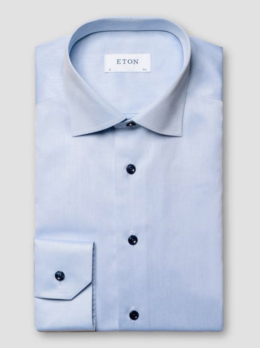 A neatly folded Eton Slim Fit Navy Details Signature Twill Dress Shirt in Light Blue, featuring a pointed collar and dark buttons with the "ETON" label, is displayed against a plain light background.