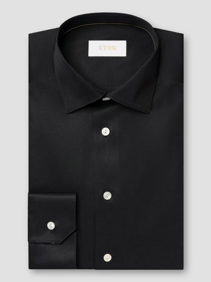 The Eton Contemporary Fit Solid Elevated Twill Dress Shirt in Black features white buttons and an "ETON" label inside the collar, neatly folded and displayed on a light gray background.