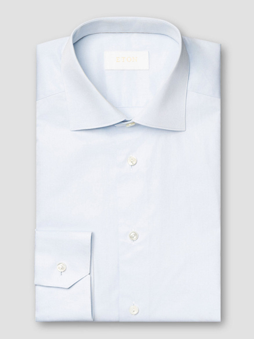 The Eton Contemporary Fit Solid Elevated Twill Dress Shirt in Light Blue features a spread collar and white buttons, neatly folded and displayed against a plain gray background.