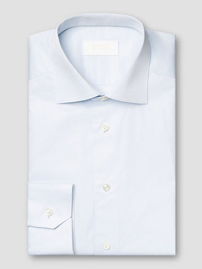 The Eton Contemporary Fit Solid Elevated Twill Dress Shirt in Light Blue features a spread collar and white buttons, neatly folded and displayed against a plain gray background.