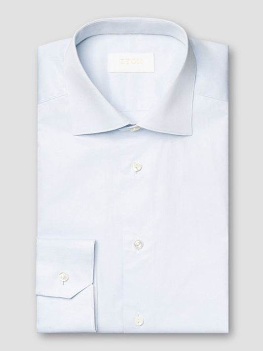 The Eton Contemporary Fit Solid Elevated Twill Dress Shirt in Light Blue features a spread collar and white buttons, neatly folded and displayed against a plain gray background.