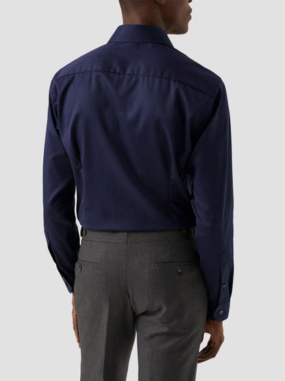 A man stands facing away, wearing an Eton Contemporary Fit Solid Signature Twill Dress Shirt in Navy Blue and gray dress pants against a plain light background.