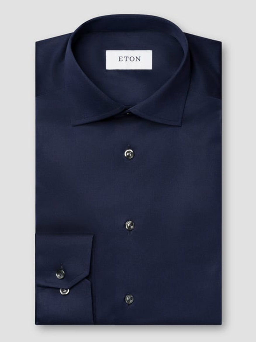 A neatly folded Eton Contemporary Fit Solid Signature Twill Dress Shirt in navy blue with black buttons and an "ETON" label inside the collar, shown against a plain light gray background.