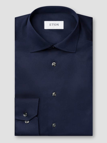 A neatly folded Eton Contemporary Fit Solid Signature Twill Dress Shirt in navy blue with black buttons and an "ETON" label inside the collar, shown against a plain light gray background.