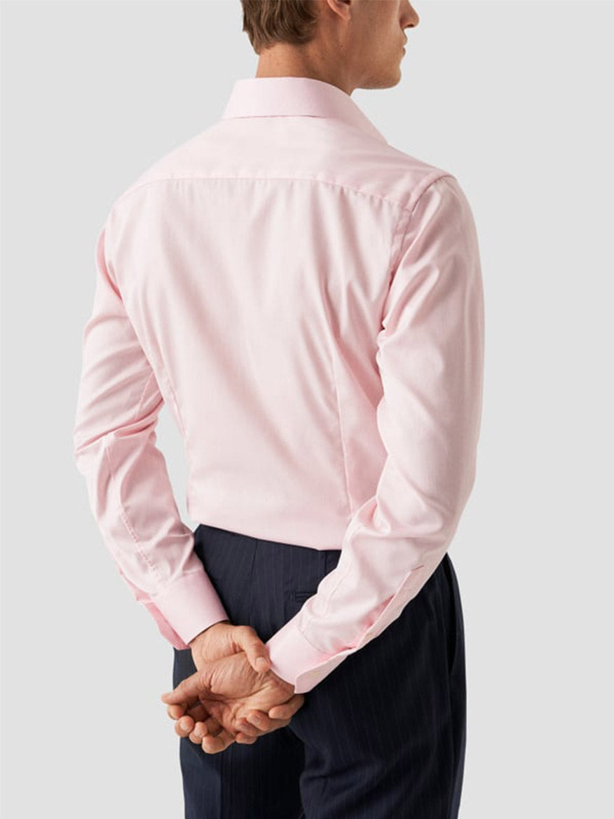 A man, seen from behind with hands clasped, wears an Eton Contemporary Fit Solid Signature Twill Dress Shirt in Pink and dark trousers.