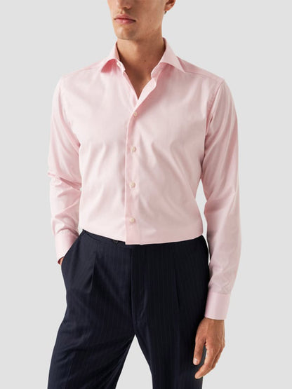 A man wears the Eton Contemporary Fit Solid Signature Twill Dress Shirt in pink with sleeves down and black pinstripe trousers, standing against a plain light gray background.