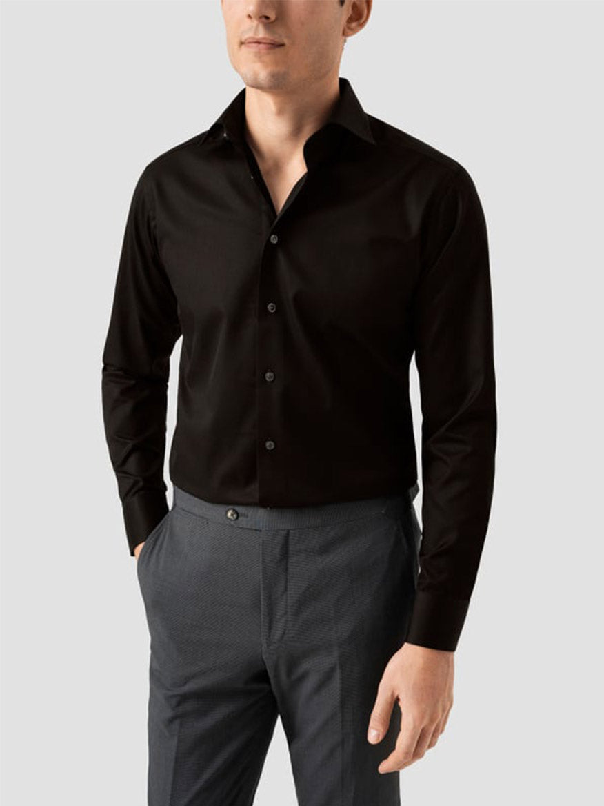 A man wearing an Eton Slim Fit Solid Signature Twill Dress Shirt in black with a cut away collar and gray trousers stands against a plain light background.
