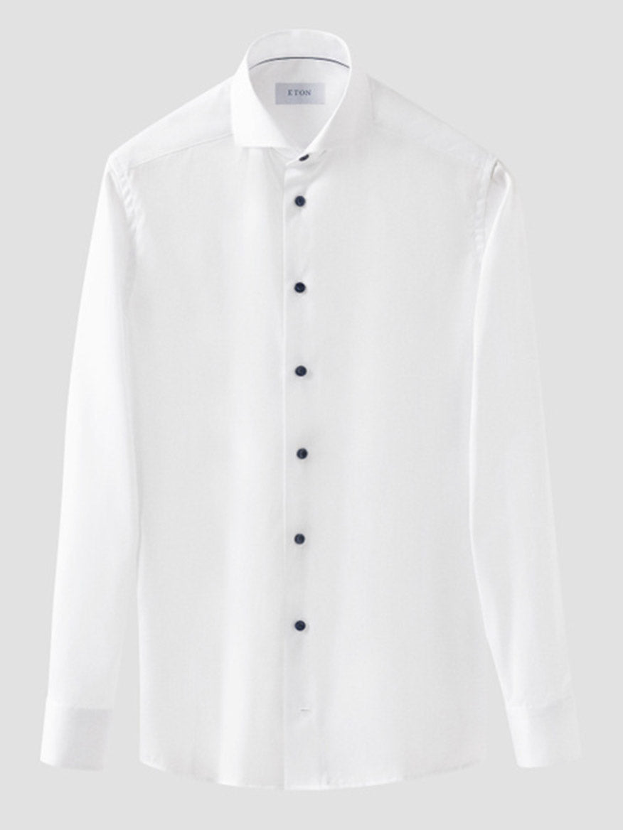 The Eton Slim Fit Solid Signature Twill Dress Shirt in white features an extreme cut away collar, navy details, and wrinkle-free fabric, shown with long sleeves and a sleek fit against a plain gray background.