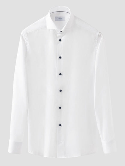 The Eton Slim Fit Solid Signature Twill Dress Shirt in white features an extreme cut away collar, navy details, and wrinkle-free fabric, shown with long sleeves and a sleek fit against a plain gray background.