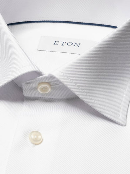 Close-up of an Eton Contemporary Fit Solid Textured Twill Dress Shirt in white, featuring a pointed collar, buttoned placket, single cuff, and inner label with the brand name “ETON.”.