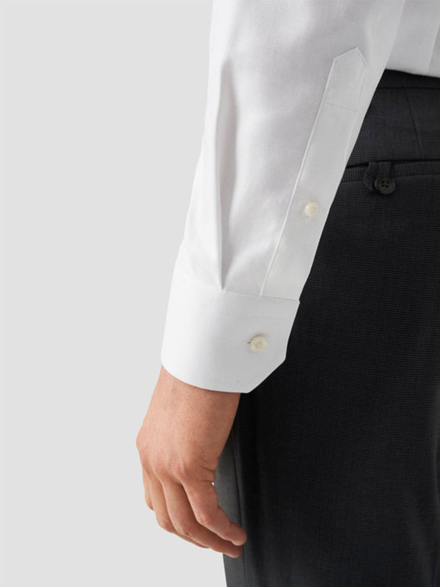 A person wearing the Eton Contemporary Fit Solid Textured Twill Dress Shirt in White, paired with dark trousers, their left arm relaxed at their side, shown from mid-torso down.