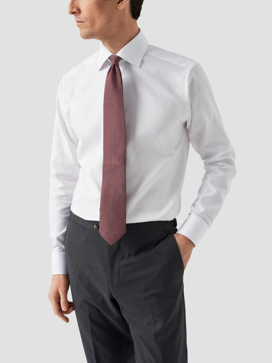 A man in an Eton Contemporary Fit Solid Textured Twill Dress Shirt in White with a red patterned tie and dark grey trousers stands against a plain light grey background.