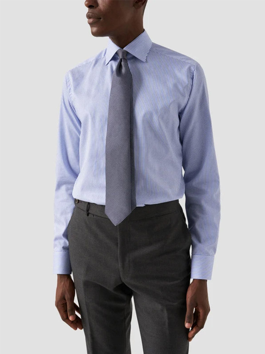 A man wears the Eton Contemporary Fit Striped Fine Twill Dress Shirt in Light Blue, paired with a grey patterned tie and dark grey trousers, standing against a plain light background.