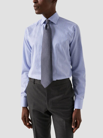 A man wears the Eton Contemporary Fit Striped Fine Twill Dress Shirt in Light Blue, paired with a grey patterned tie and dark grey trousers, standing against a plain light background.