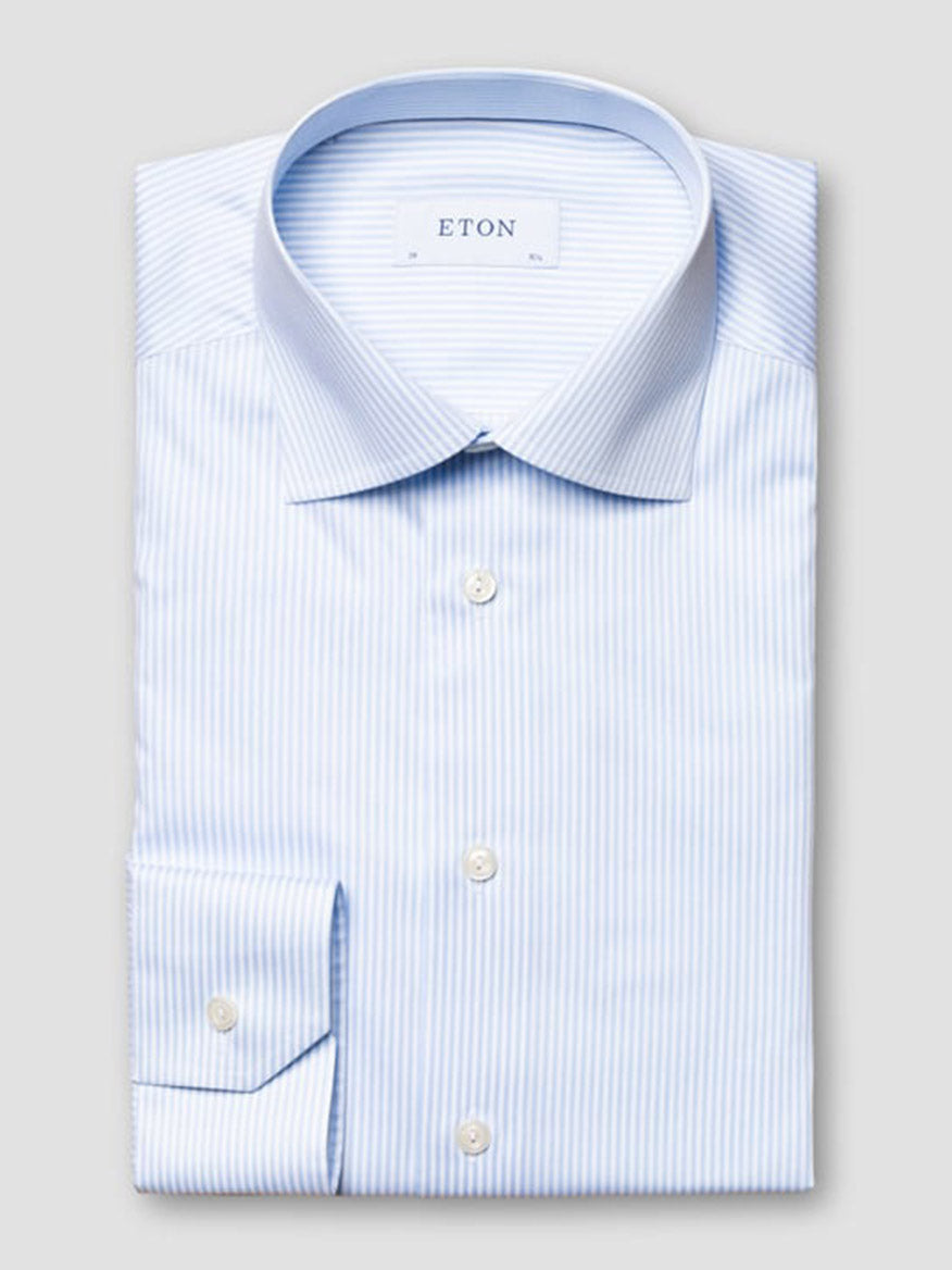 A neatly folded Eton Slim Fit Striped Fine Twill Dress Shirt in light blue with a cut away collar, featuring white bengal stripes and buttoned cuffs, labeled "ETON" on the inside collar.