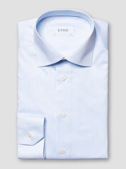 A neatly folded Eton Slim Fit Striped Fine Twill Dress Shirt in light blue with a cut away collar, featuring white bengal stripes and buttoned cuffs, labeled "ETON" on the inside collar.