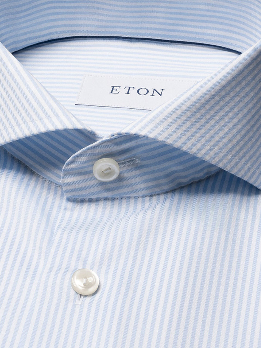 Close-up of an Eton Slim Fit Striped Fine Twill Dress Shirt in light blue, featuring white buttons, an extreme cut away collar, and a visible brand label. This modern style updates classic shirting with subtle Bengal stripes.
