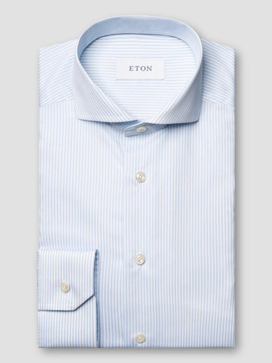 A neatly folded Eton Slim Fit Striped Fine Twill Dress Shirt in light blue with white stripes, featuring an extreme cut away collar and button cuffs, labeled “ETON” inside the collar.