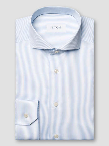 A neatly folded Eton Slim Fit Striped Fine Twill Dress Shirt in light blue with white stripes, featuring an extreme cut away collar and button cuffs, labeled “ETON” inside the collar.