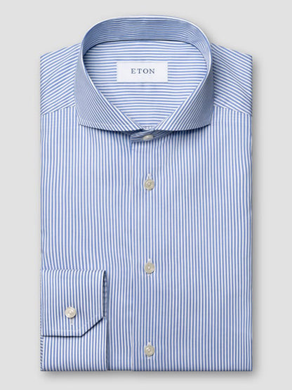 A neatly folded Eton Slim Fit Striped Fine Twill Dress Shirt in mid blue, featuring an extreme cut away collar, long sleeves, white buttons, and classic blue and white bengal stripes.