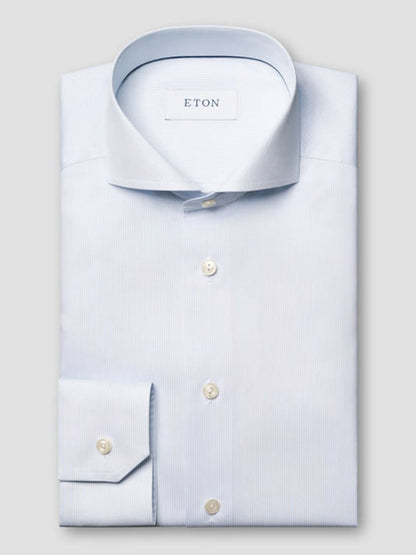 A light blue Eton Slim Fit Striped Twill Dress Shirt is neatly folded, featuring a spread collar, buttoned cuffs, and pearl-colored buttons against a plain background.