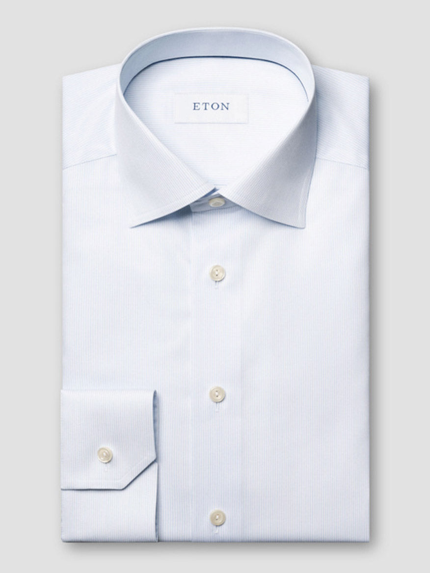 A neatly folded Eton Slim Fit Striped Twill Dress Shirt in light blue, featuring a pointed collar and buttoned cuffs, is displayed on a flat surface with the "ETON" label visible inside the collar.