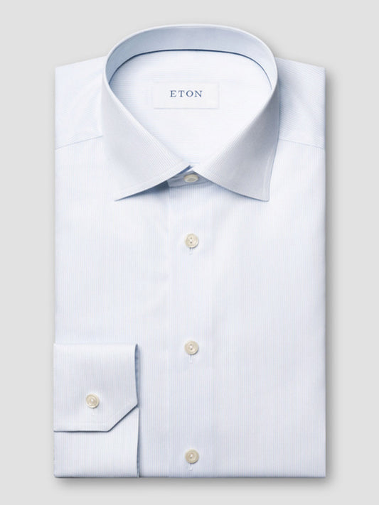 A neatly folded Eton Slim Fit Striped Twill Dress Shirt in light blue, featuring a pointed collar and buttoned cuffs, is displayed on a flat surface with the "ETON" label visible inside the collar.