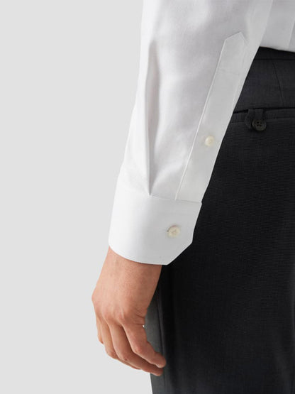 A person wears the Eton Slim Fit Solid Textured Twill Dress Shirt in White—Single Cuff, paired with dark trousers. Their relaxed left arm highlights the shirt’s classic business style, visible cuff, and buttons.